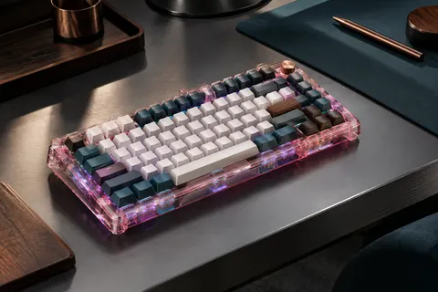Clavier mécanique compact 75 % au boîtier transparent rose, posé sur un bureau sobre avec éclairage RGB.