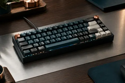Clavier mécanique compact noir à touches PBT, éclairage RVB et commande de volume sur un bureau sobre.