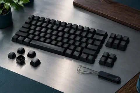 Jeu de capuchons noirs en PBT au profil OEM, disposés en rangées avec un extracteur sur un bureau sobre.